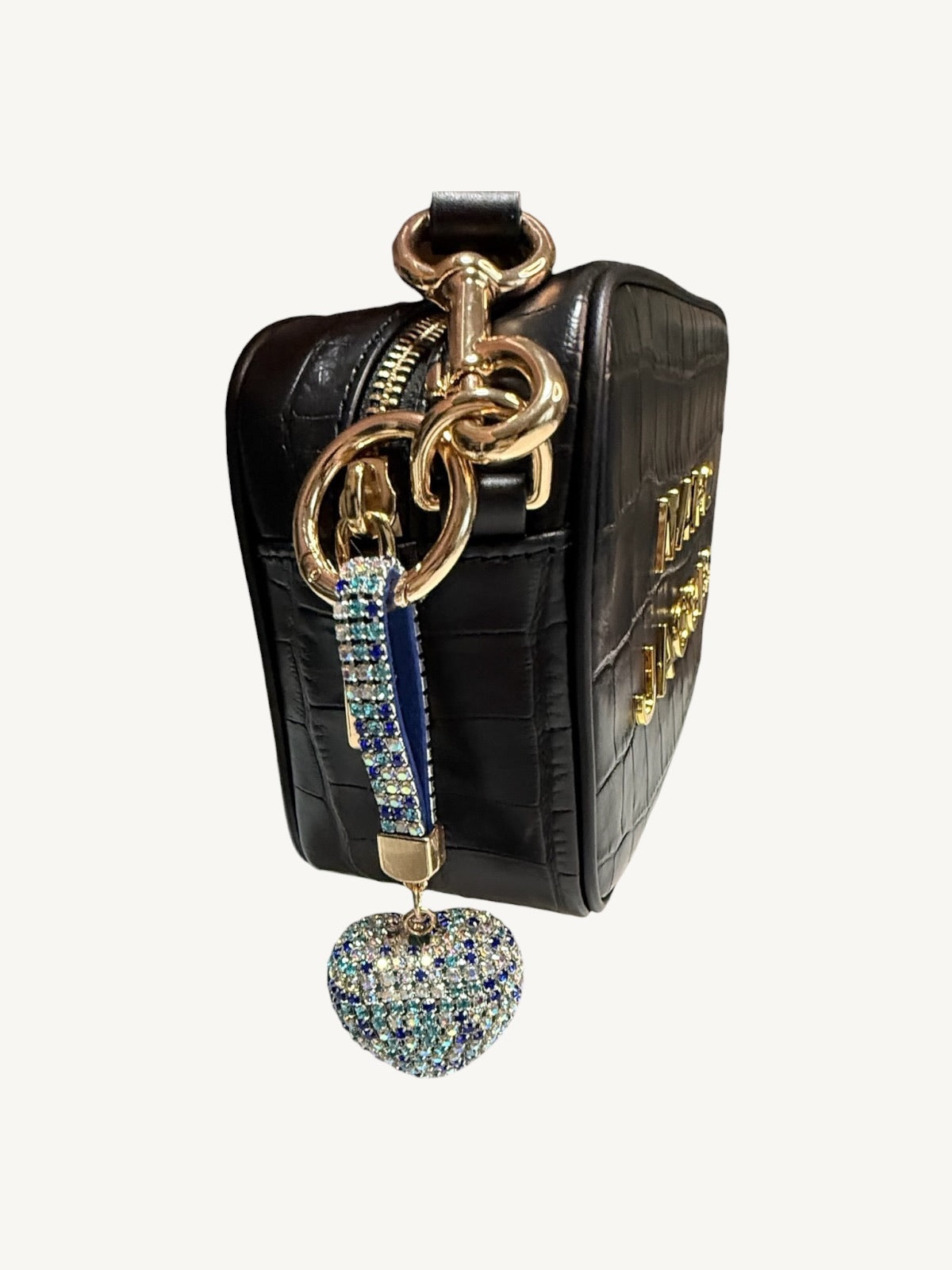 A black crocodile-embossed leather handbag with gold-tone hardware, featuring a decorative blue and gold chain strap and a dangling rhinestone-embellished heart charm, shown against a plain off-white background.