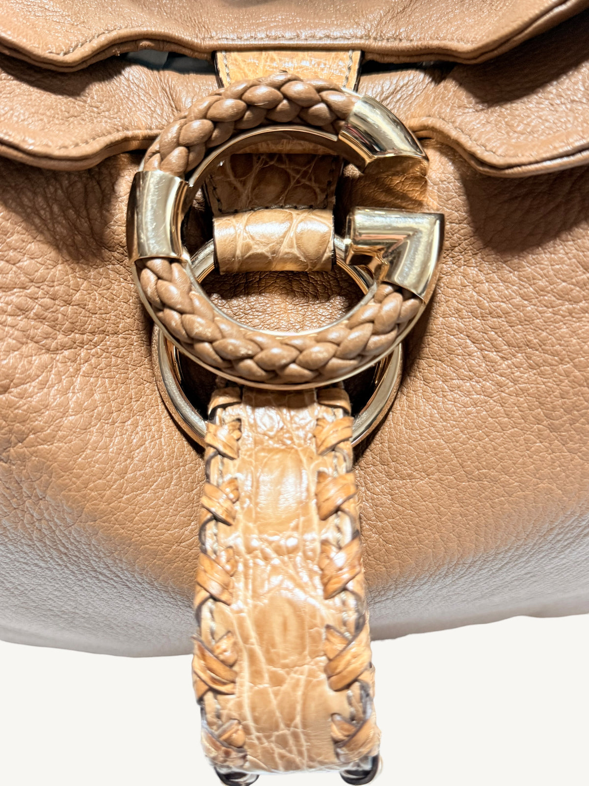 Close-up of a camel brown Gucci  leather handbag featuring a large circular G gold-tone hardware ring with braided leather detailing and a matching braided strap hanging down.