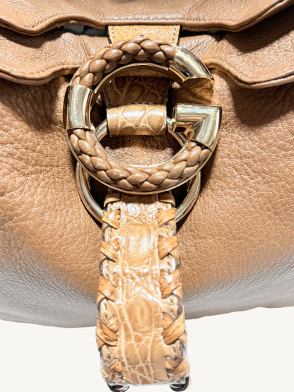 Close-up of a camel brown Gucci  leather handbag featuring a large circular G gold-tone hardware ring with braided leather detailing and a matching braided strap hanging down.