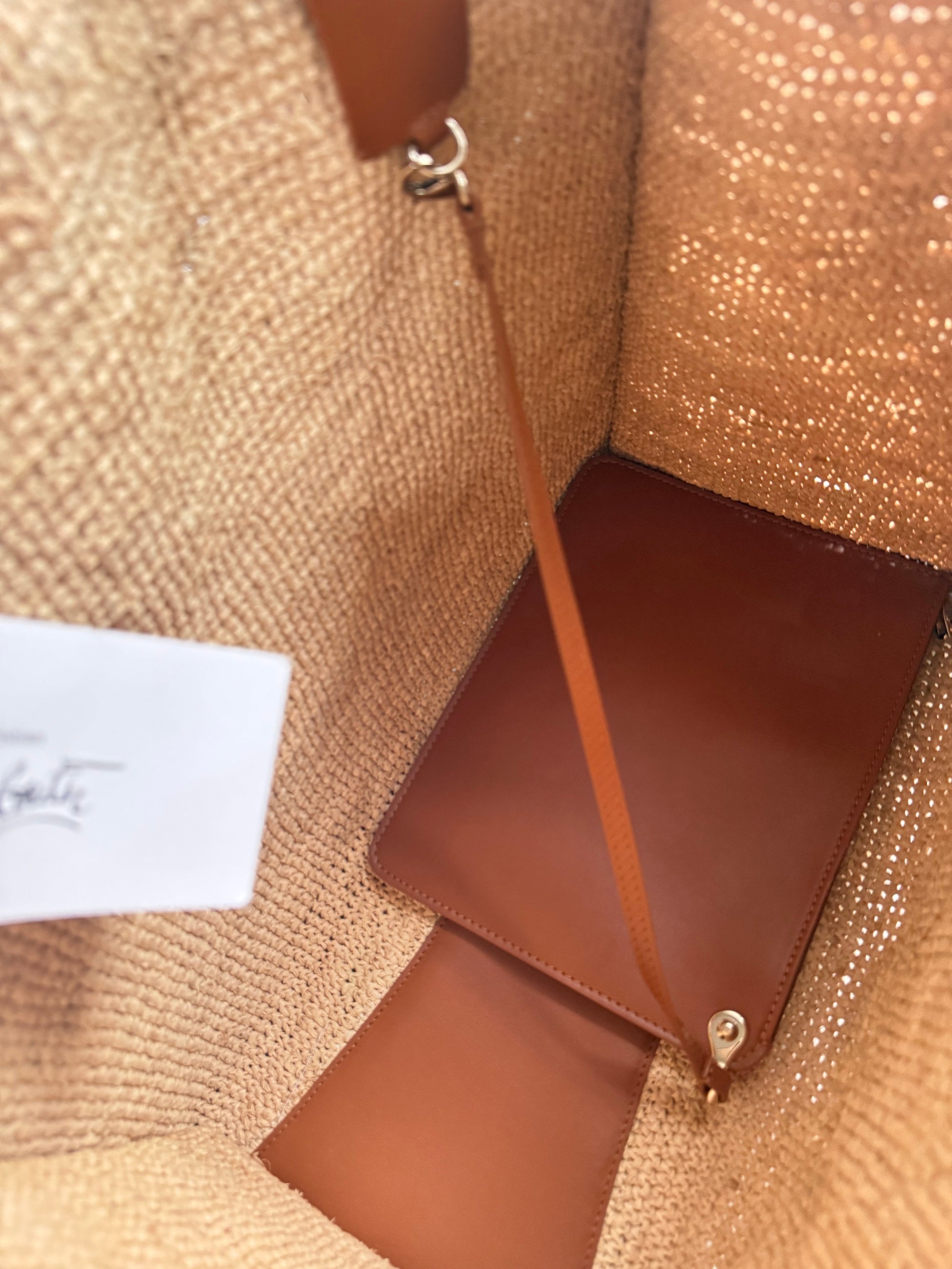Close-up of Christian Louboutin CL monogram debossed in cuoio calfskin leather on raffia tote