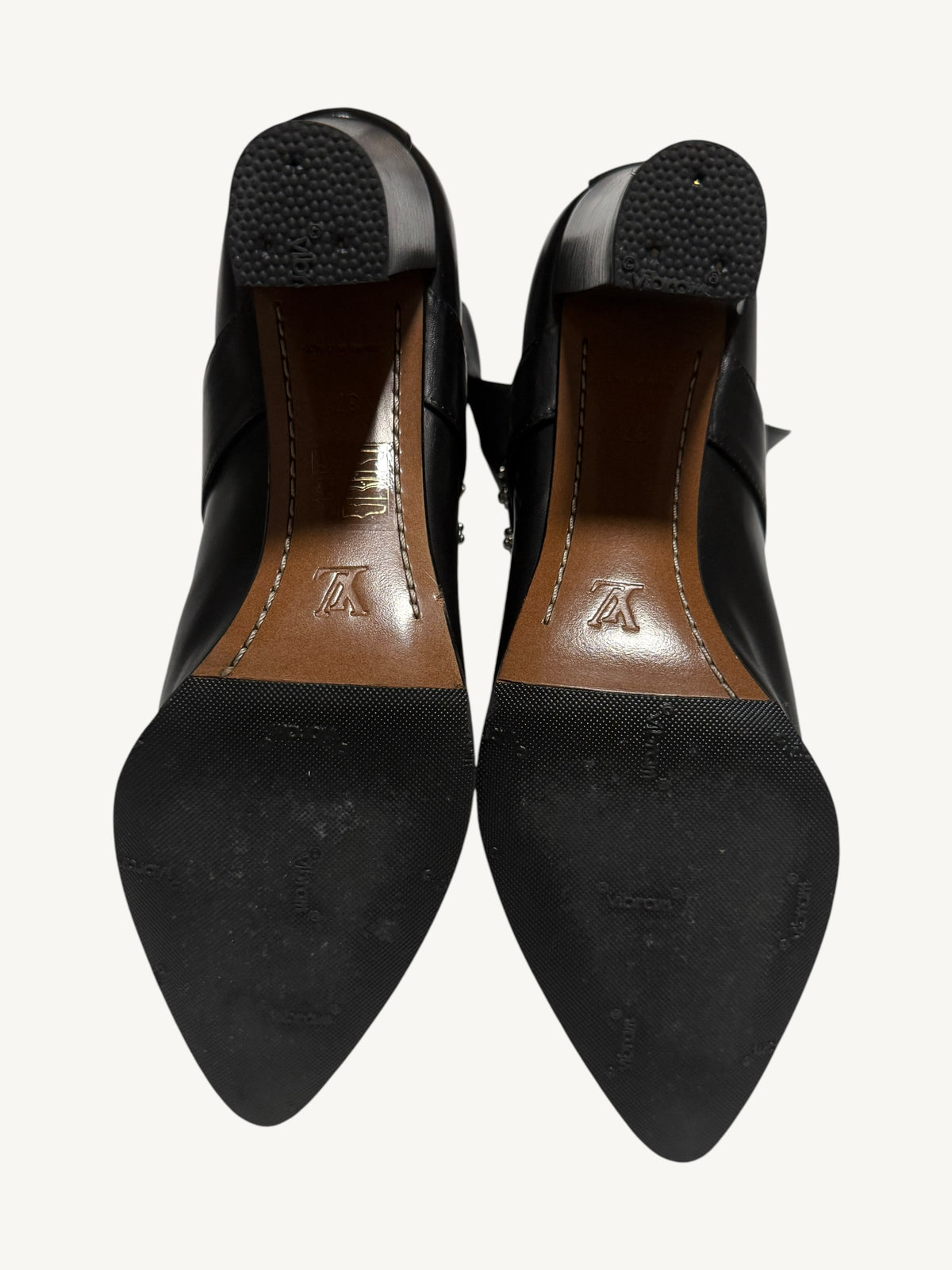 Soles of both Louis Vuitton boots, showing black rubber half-soles, textured heel caps and brown leather arches.
