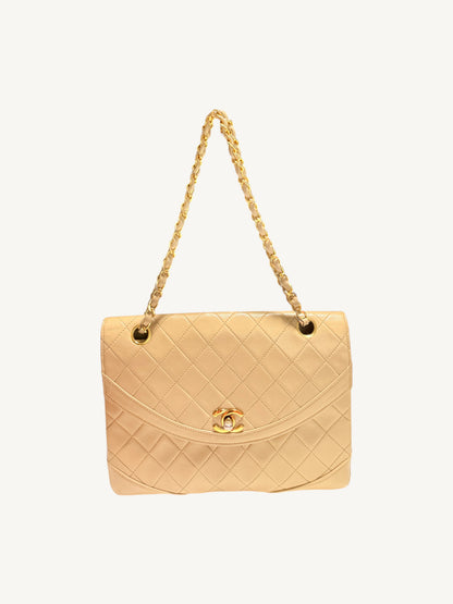 A light beige quilted Chanel leather handbag with a gold-tone chain strap and a gold interlocking CC logo clasp, shown against a plain off-white background.