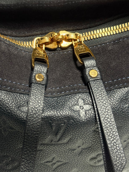 Close-up of a Louis Vuitton monogram leather bag with gold-tone zipper pulls and hardware, showing the textured black leather and embossed LV pattern.