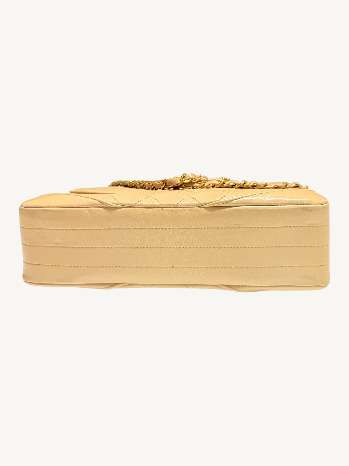 A light beige quilted leather Chanel bag with a gold chain strap, shown from the side against a plain off-white background.