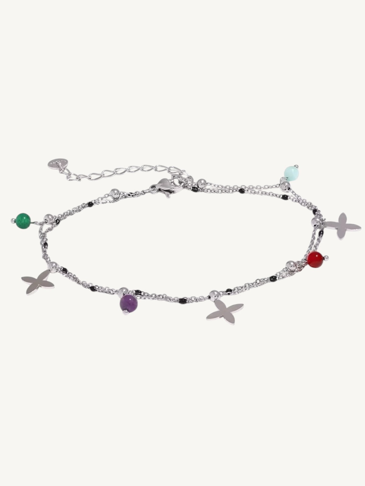 A silver-toned beaded anklet featuring butterfly and starfish charms, accented with small colorful gemstones in green, purple, red, and light blue, displayed on a light cream background.