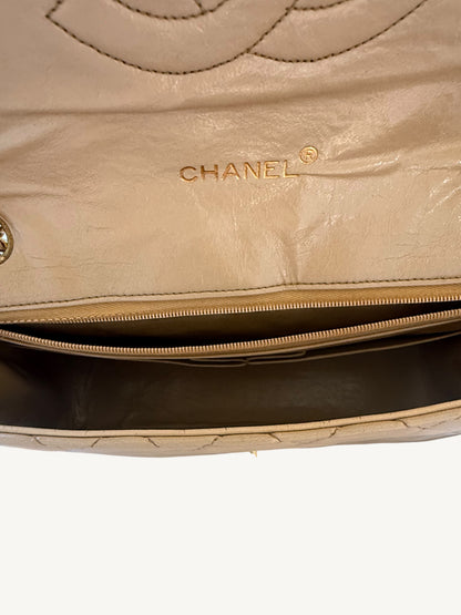 Close-up of a beige Chanel handbag interior showing the gold-embossed CHANEL logo on the leather flap and a gold-tone zipper.