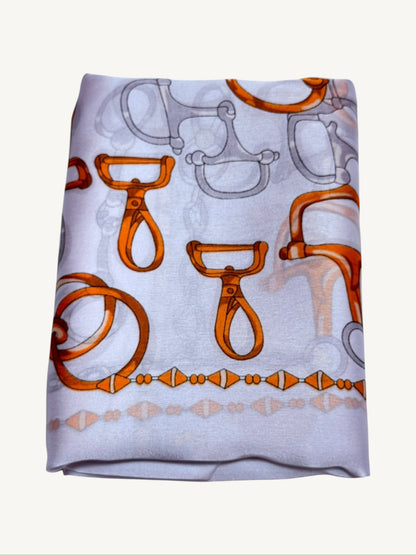 The Deauville – equestrian print silky satin scarf folded showing white base with orange hardware motifs