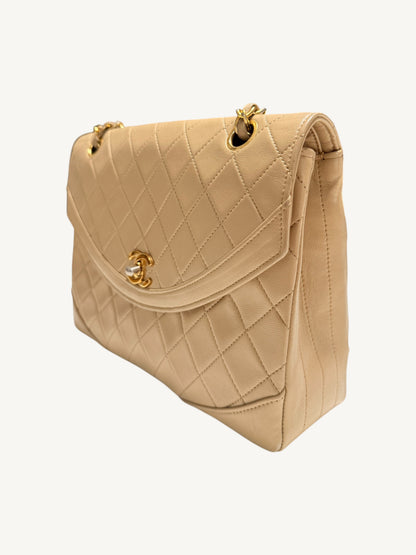 A beige quilted leather Chanel handbag with gold-tone hardware and a turn-lock closure, shown from a three-quarters angle against a plain off-white background.