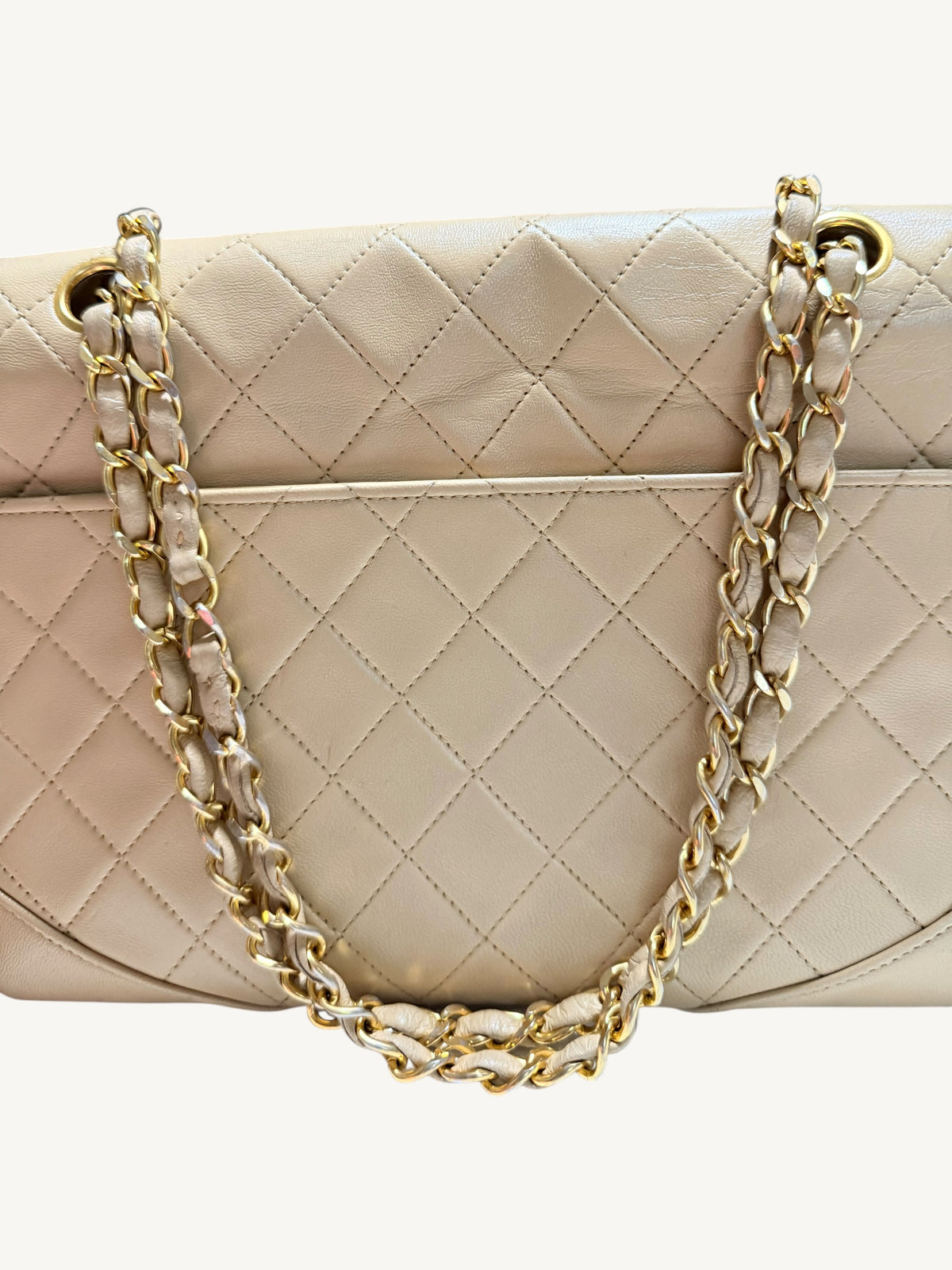 A close-up of a quilted beige Chanel leather handbag with gold-tone chain and leather handles, set against a plain light background.