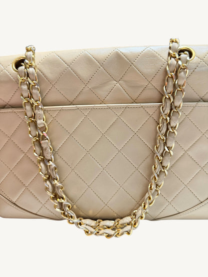 A close-up of a quilted beige Chanel leather handbag with gold-tone chain and leather handles, set against a plain light background.