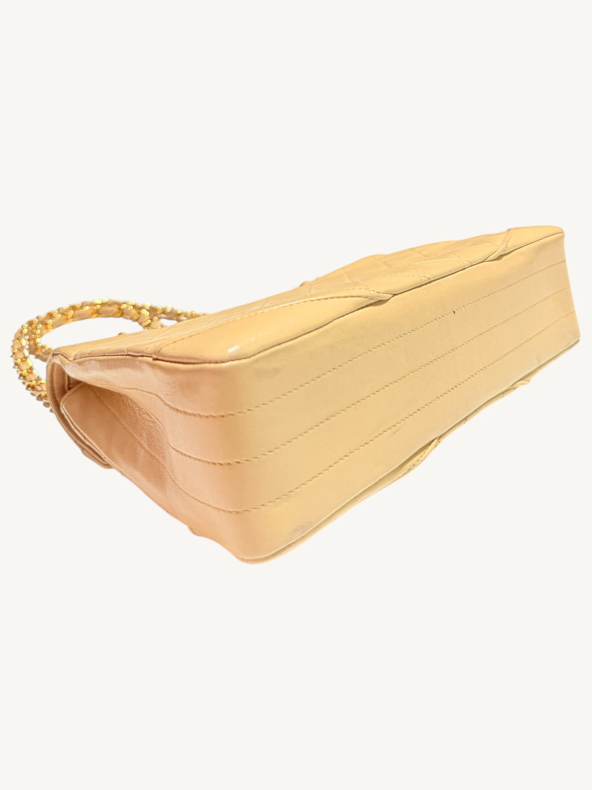 A light beige patent leather shoulder bag with a quilted top handle and a gold chain-link strap, shown from a side angle on a plain off-white background.