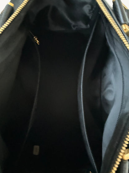 Close-up view of the interior of a black handbag, showing a black fabric lining, two central zip compartments, and gold-tone zipper hardware.
