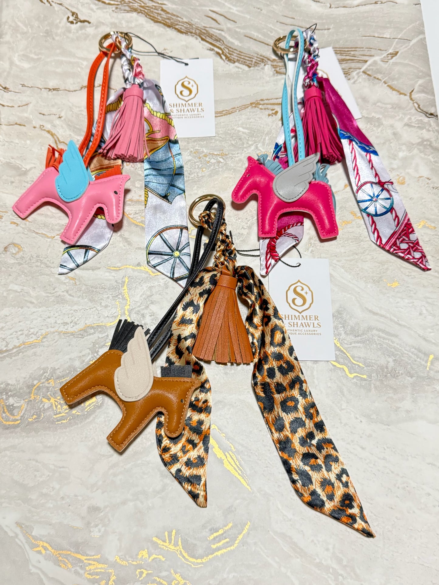 Three western-themed keychains by Thamer Saddles, each featuring a leather unicorn charm, a silk scarf, and a tassel, displayed on a light marble background.