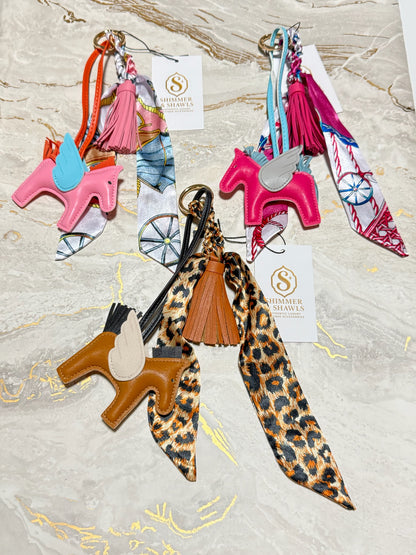 Three western-themed keychains by Thamer Saddles, each featuring a leather unicorn charm, a silk scarf, and a tassel, displayed on a light marble background.