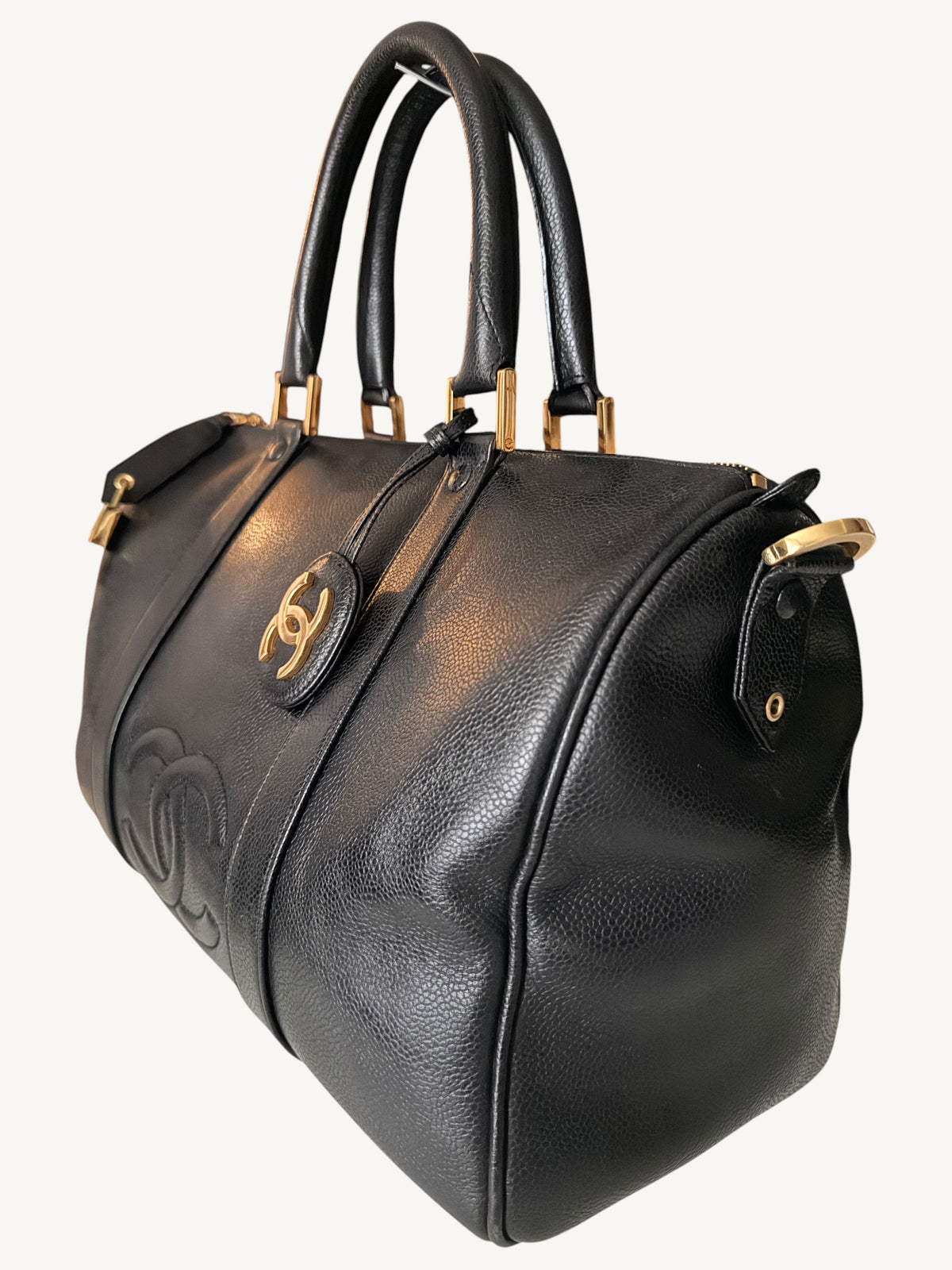 A black leather Chanel handbag with gold-tone hardware, featuring the iconic interlocking CC logo on the front and embossed CC detailing on the side, set against a plain off-white background.