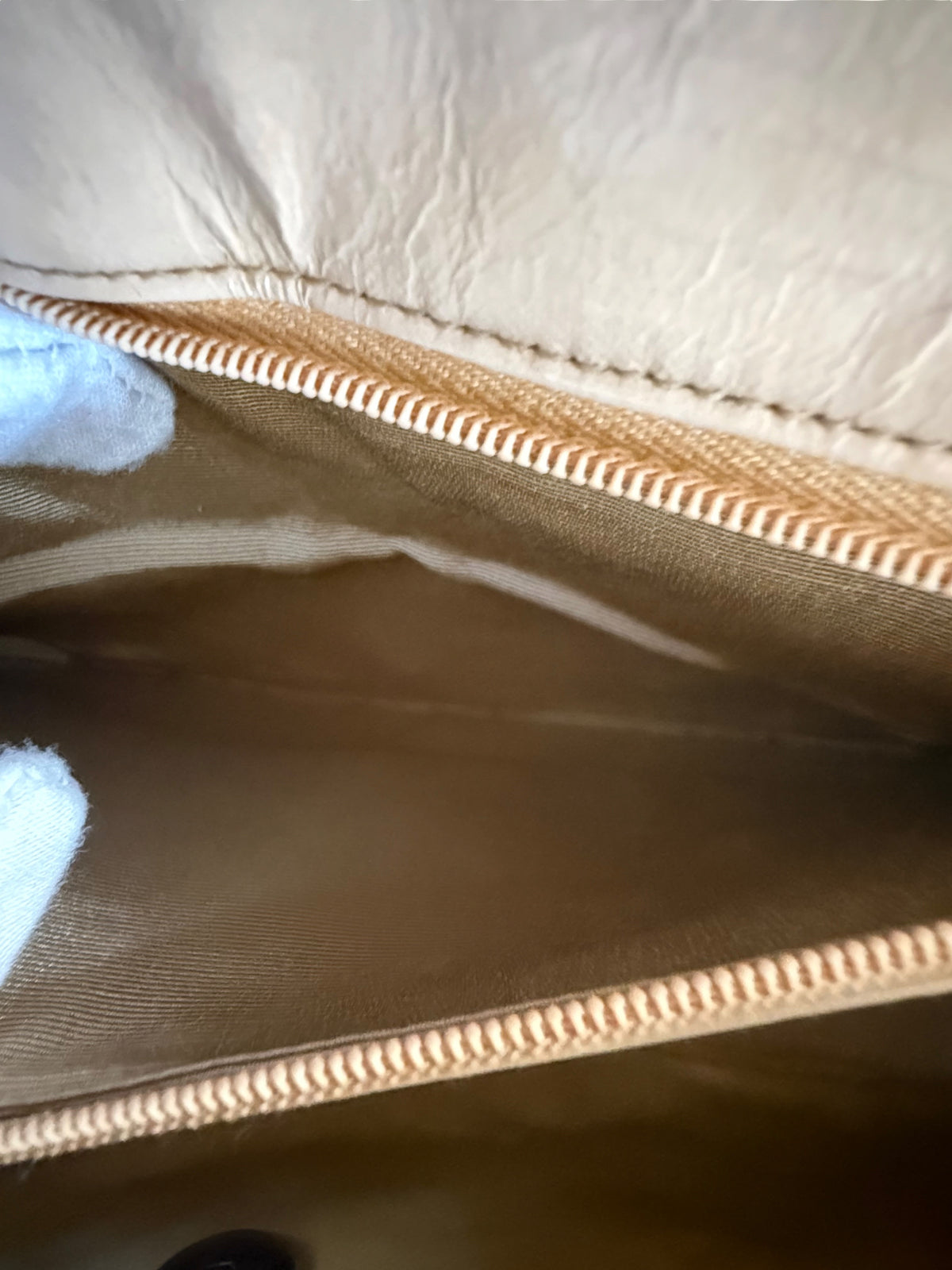 Close-up of the interior of a beige Chanel leather bag, showing the tan lining and a gold-toned zipper.