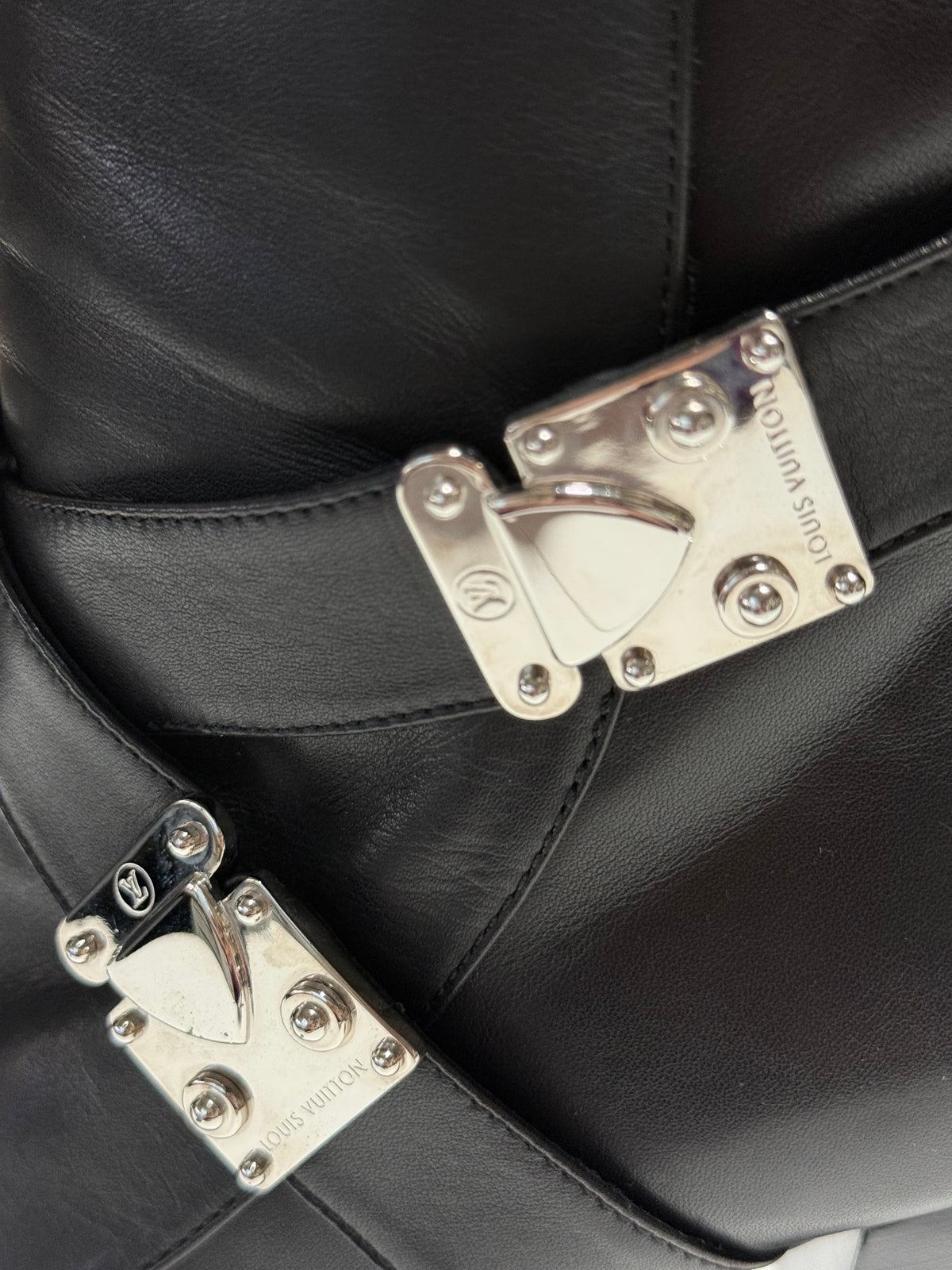 Close-up of two silver-tone S-Lock clasps with Louis Vuitton engravings on black leather straps.
