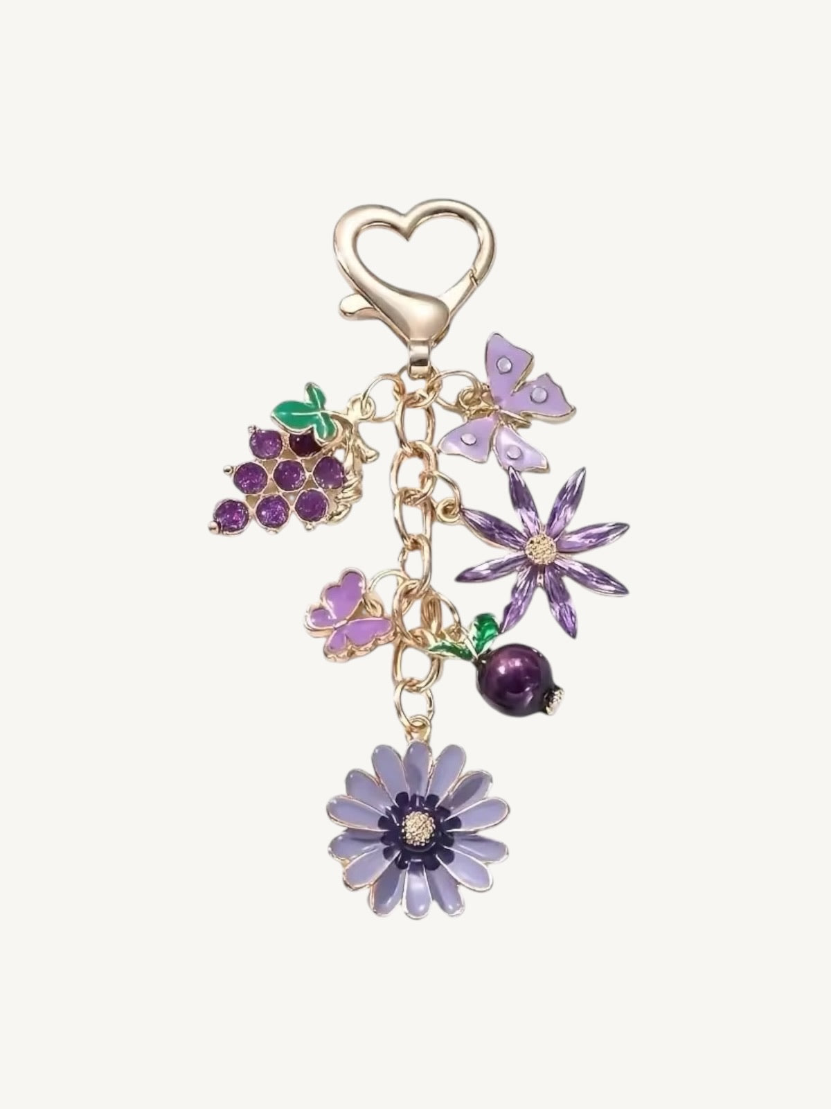 A gold-tone charm keychain featuring purple enamel flowers, a grapevine cluster, and a purple berry, attached to a heart-shaped clasp on a light cream background.