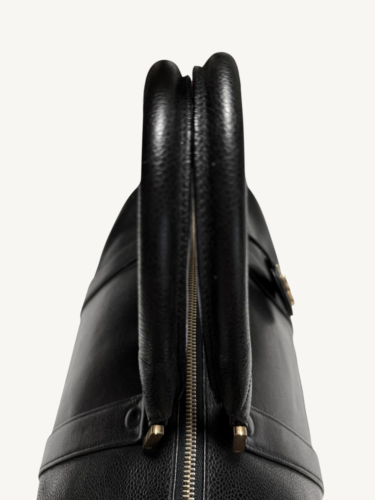 Close-up of a black CHANEL leather handbag showing the top handle, double zipper closure, and gold-tone hardware against a plain light background.