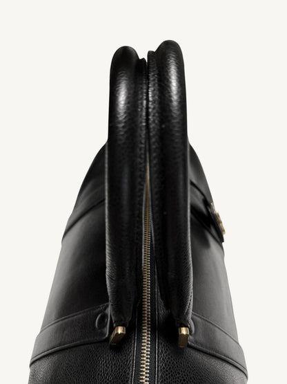 Close-up of a black CHANEL leather handbag showing the top handle, double zipper closure, and gold-tone hardware against a plain light background.