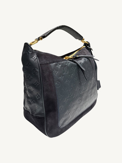 Louis Vuitton Audacieuse MM Infini — three-quarter side view showing monogram empreinte embossing, suede panels, gold zipper hardware and flat leather top handle

