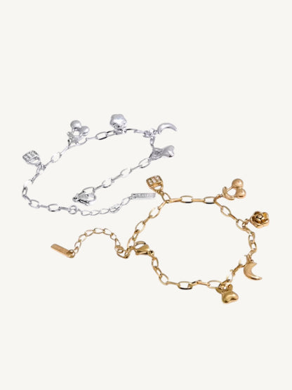 Two delicate chain bracelets with small charms, one in silver-tone metal and one in gold-tone metal, displayed on a light cream background.