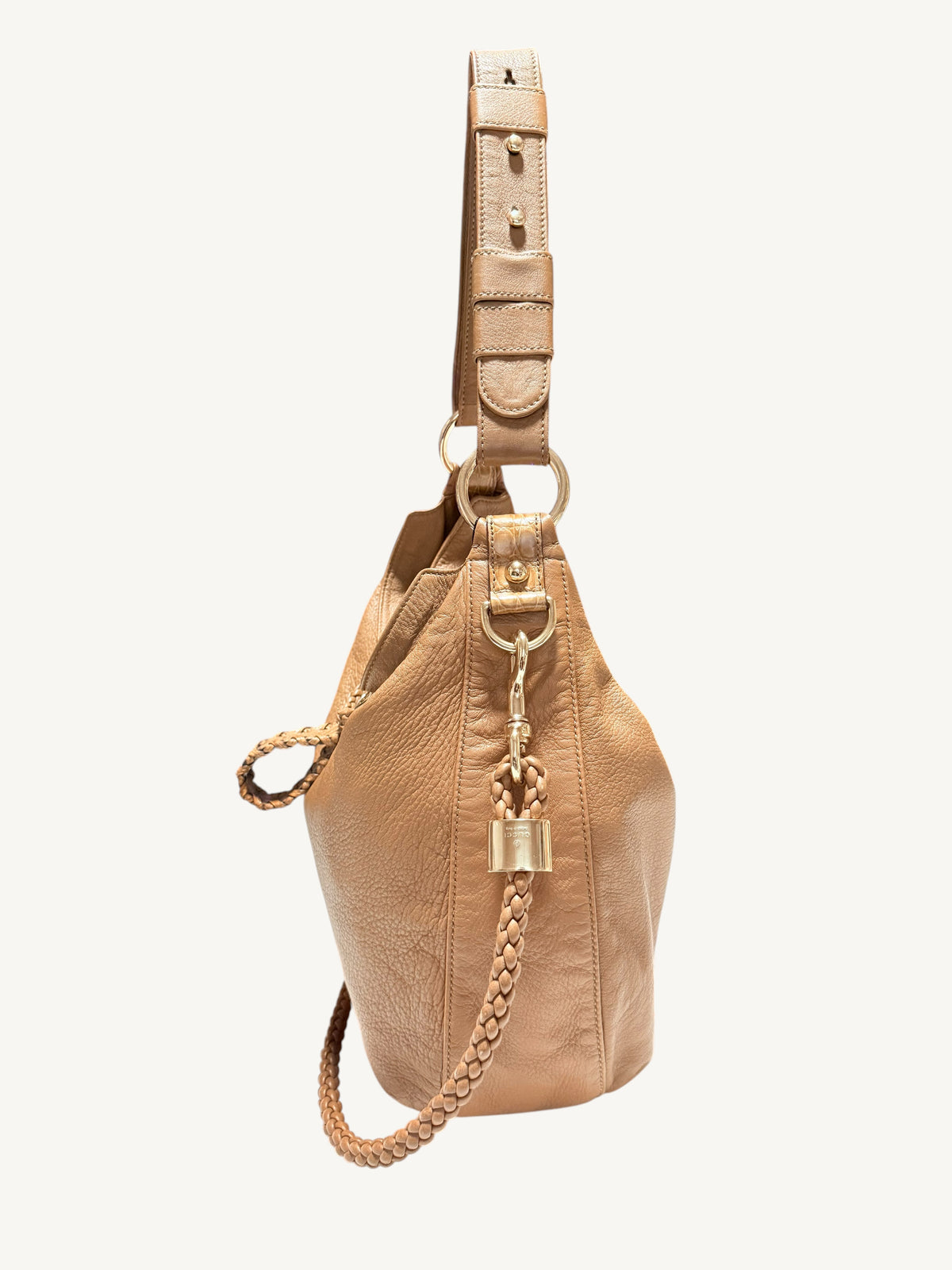 A camel brown Gucci leather bucket bag with a matching shoulder strap, gold-tone hardware, and a decorative padlock charm, shown against a plain off-white background.