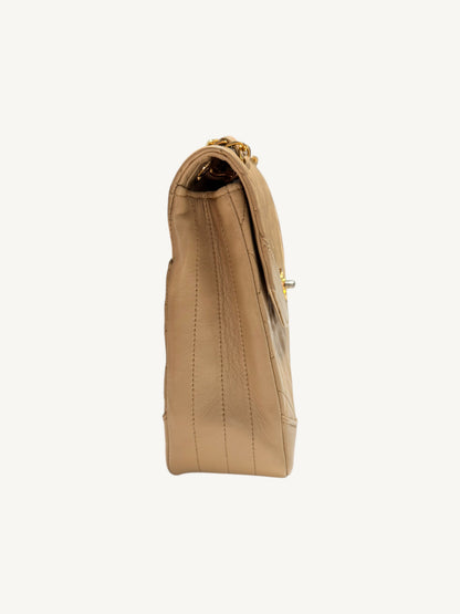A side profile view of a beige Chanel leather handbag with gold-tone hardware, shown against a plain off-white background.