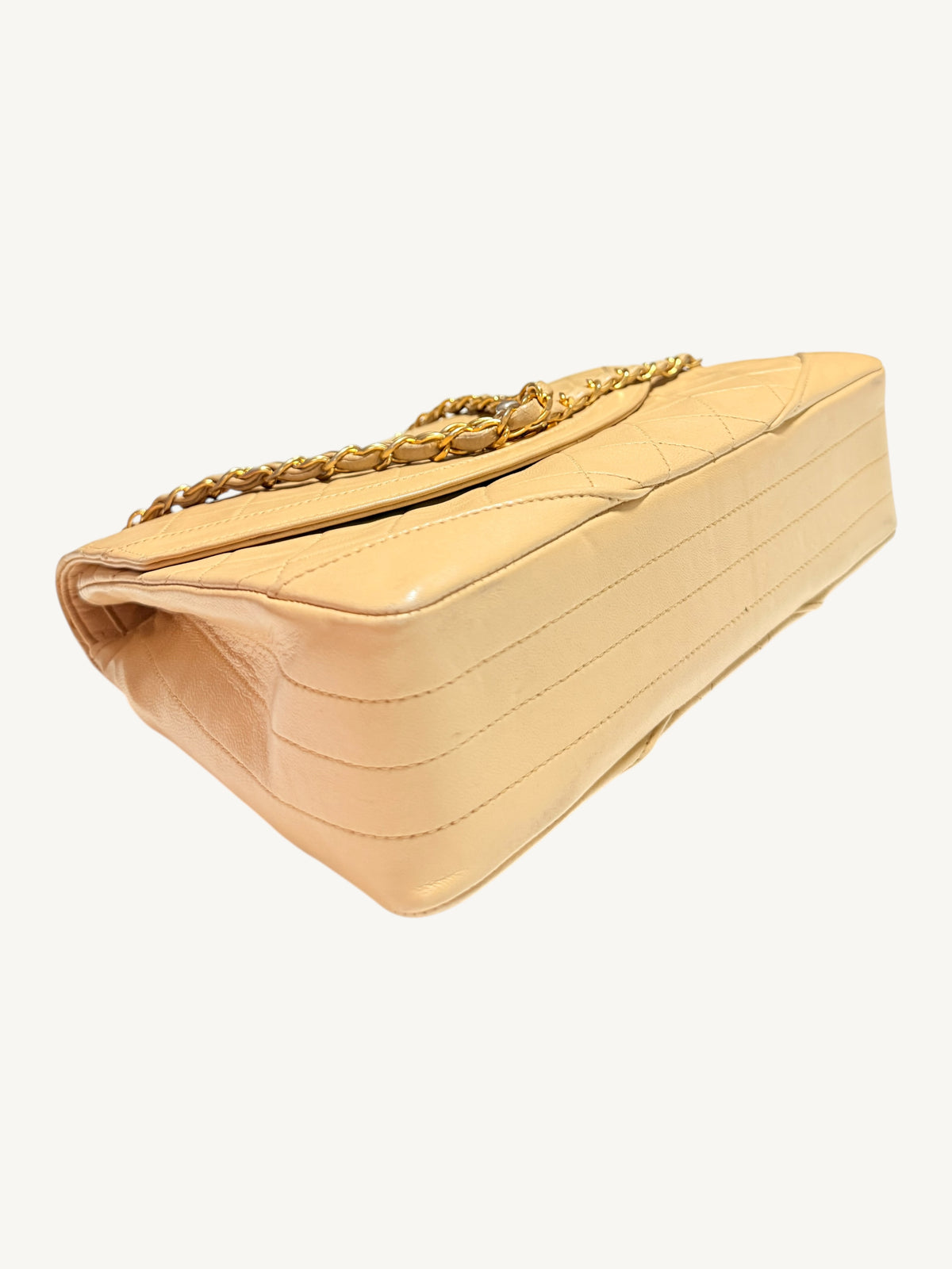 A beige quilted leather shoulder bag with a gold chain strap, shown from a three-quarters perspective against a plain off-white background.