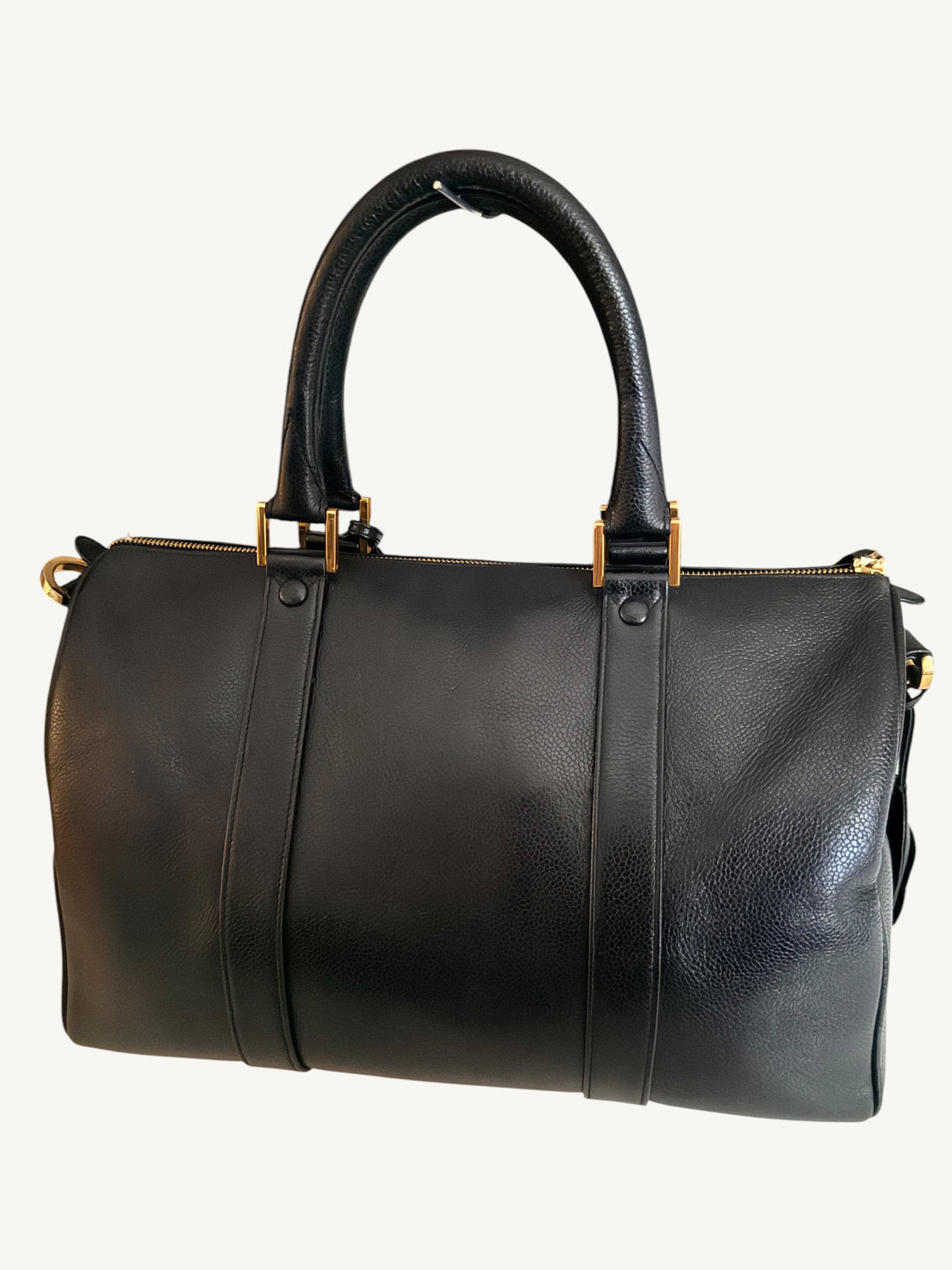 A black leather duffel bag with double top handles and gold-tone hardware, shown against a plain off-white background.