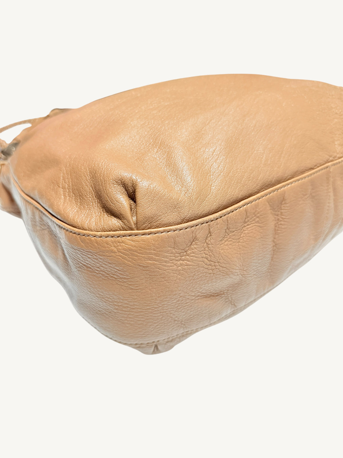 A close-up of a camel brown Gucci  leather shoulder bag showing the textured grain and stitched edge against a plain off-white background.