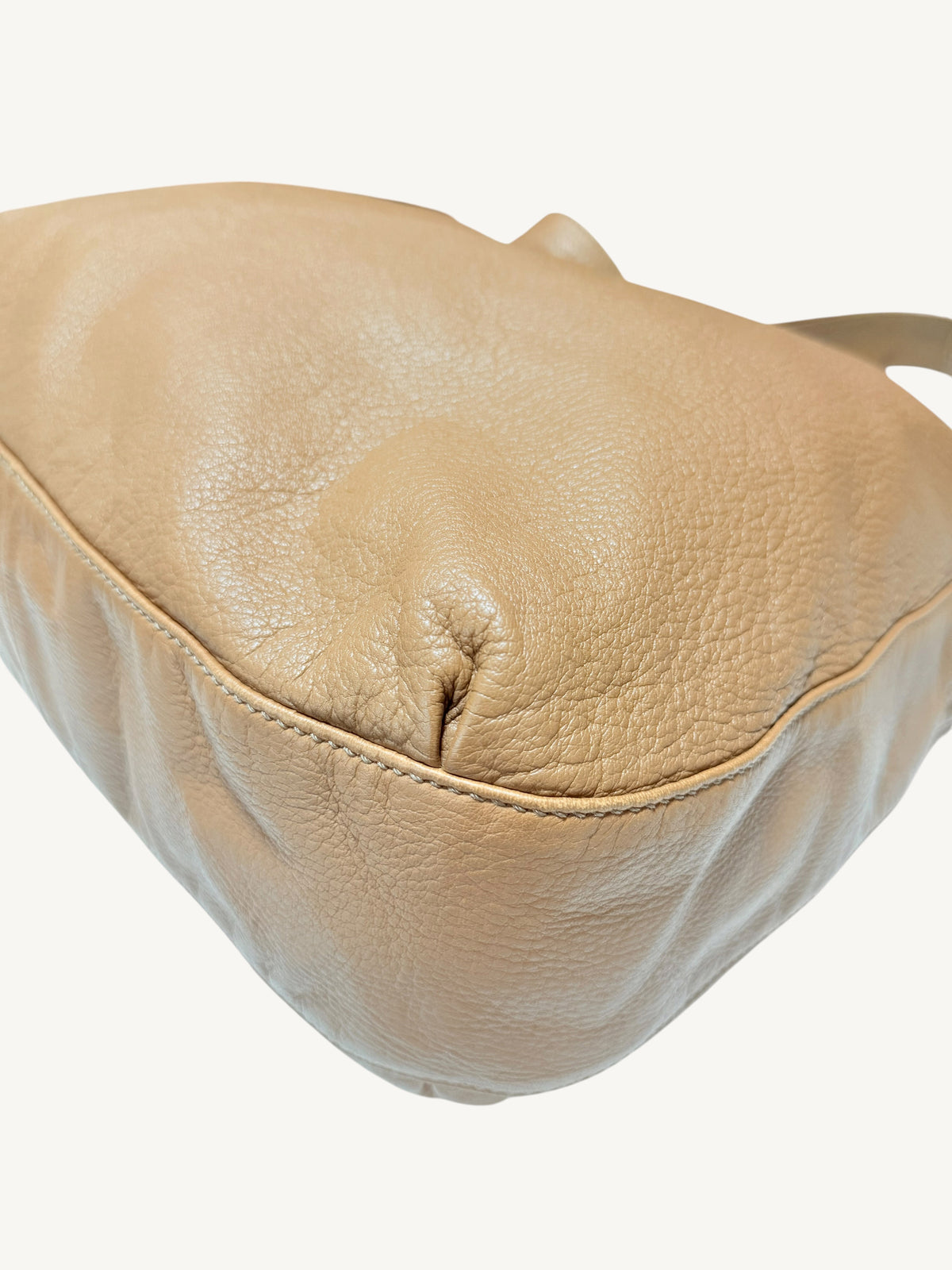 A close-up of a camel brown Gucci pebbled leather shoulder bag against a clean off-white background.