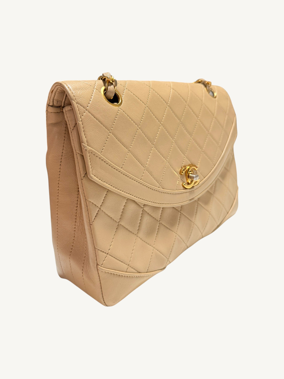 A beige quilted leather  Chanel handbag with gold-tone hardware, shown from a three-quarters angle against a plain off-white background.