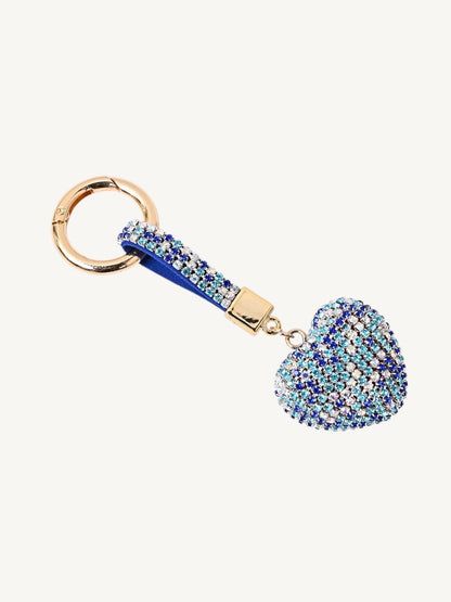 A rhinestone-embellished keychain featuring a heart-shaped charm, a blue fabric loop, and gold-tone metal hardware, shown on a plain off-white background.