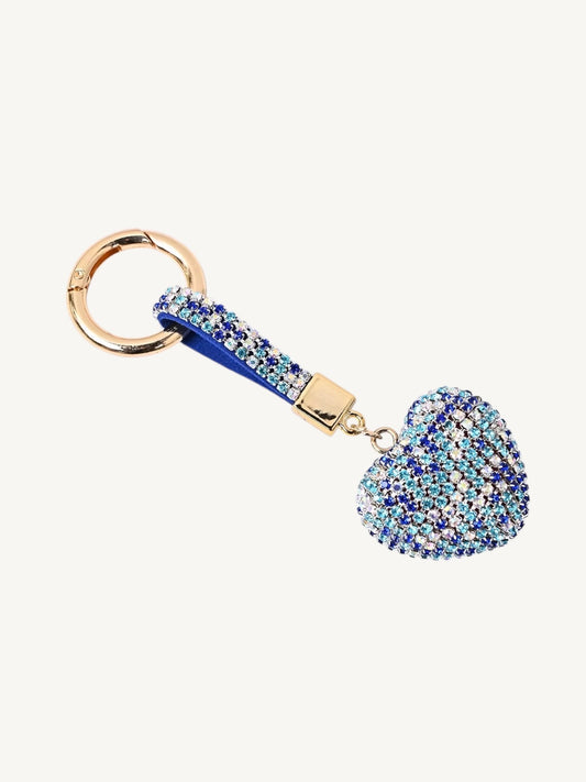 A rhinestone-embellished keychain featuring a heart-shaped charm, a blue fabric loop, and gold-tone metal hardware, shown on a plain off-white background.