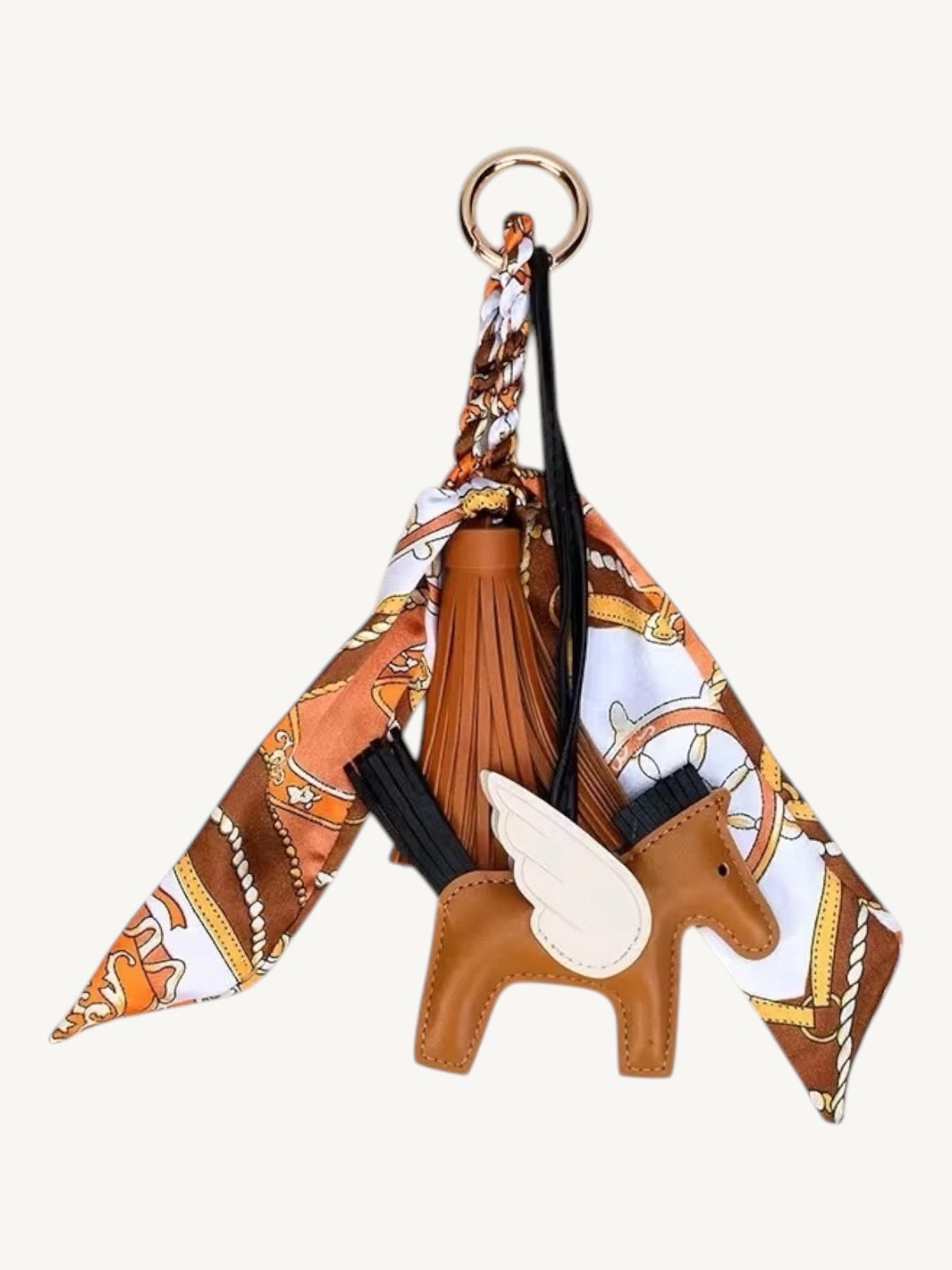 A fashion keychain charm featuring a brown leather winged horse figure, a brown leather tassel, a gold-tone key ring, and a patterned silk scarf in brown, white, and orange.