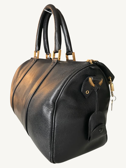 A black pebbled leather CHANEL duffel bag with gold-tone hardware, dual top handles, and a hanging leather tag, shown on a plain light background.