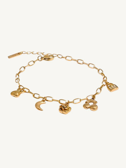 A gold chain bracelet with multiple dangling charms, including a crescent moon, rose, cloud, and small heart, displayed on a light cream background.