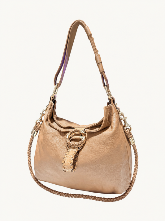 A brown leather shoulder bag with a gold-tone metal ring detail and a braided strap, shown against a plain off-white background.