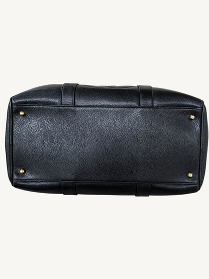The bottom view of a black pebbled CHANEL leather duffel bag with gold-tone metal studs on the corners, shown against a light off-white background.