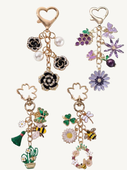 Four gold-tone charm earrings with floral and nature motifs, including roses, flowers, bees, a cactus, and pearls, displayed on a light cream background.