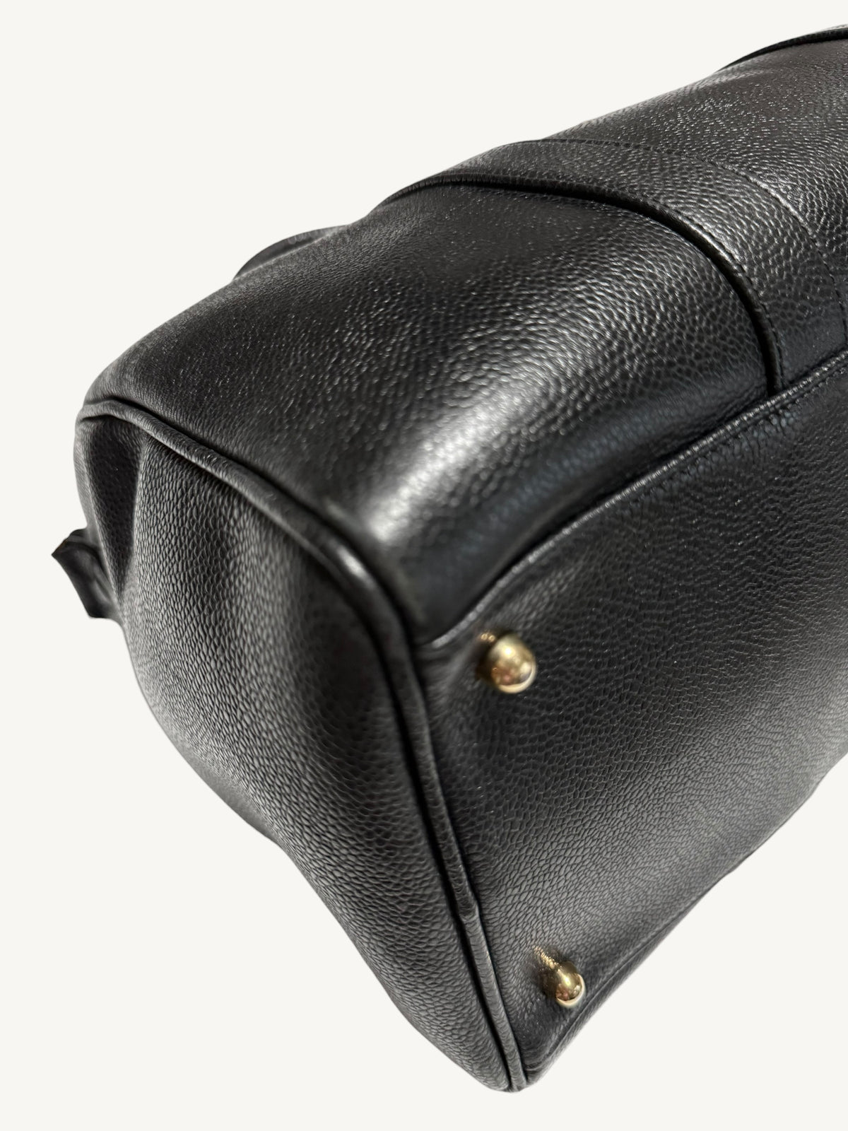Close-up of a black pebbled leather bag corner with small gold-tone metal studs, photographed on a plain light background.