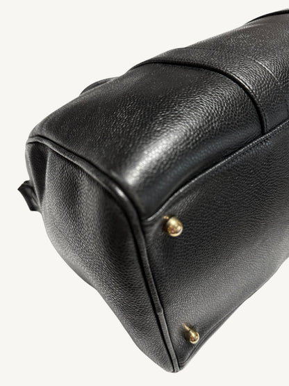 Close-up of a black pebbled leather bag corner with small gold-tone metal studs, photographed on a plain light background.