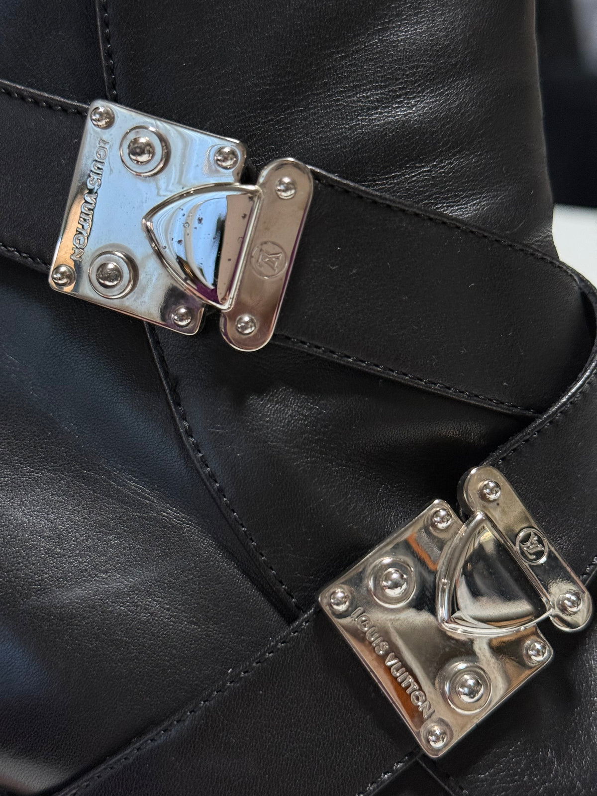 Close-up of silver-tone S-Lock hardware, showing small dark spots on the upper clasp and stitched leather straps.