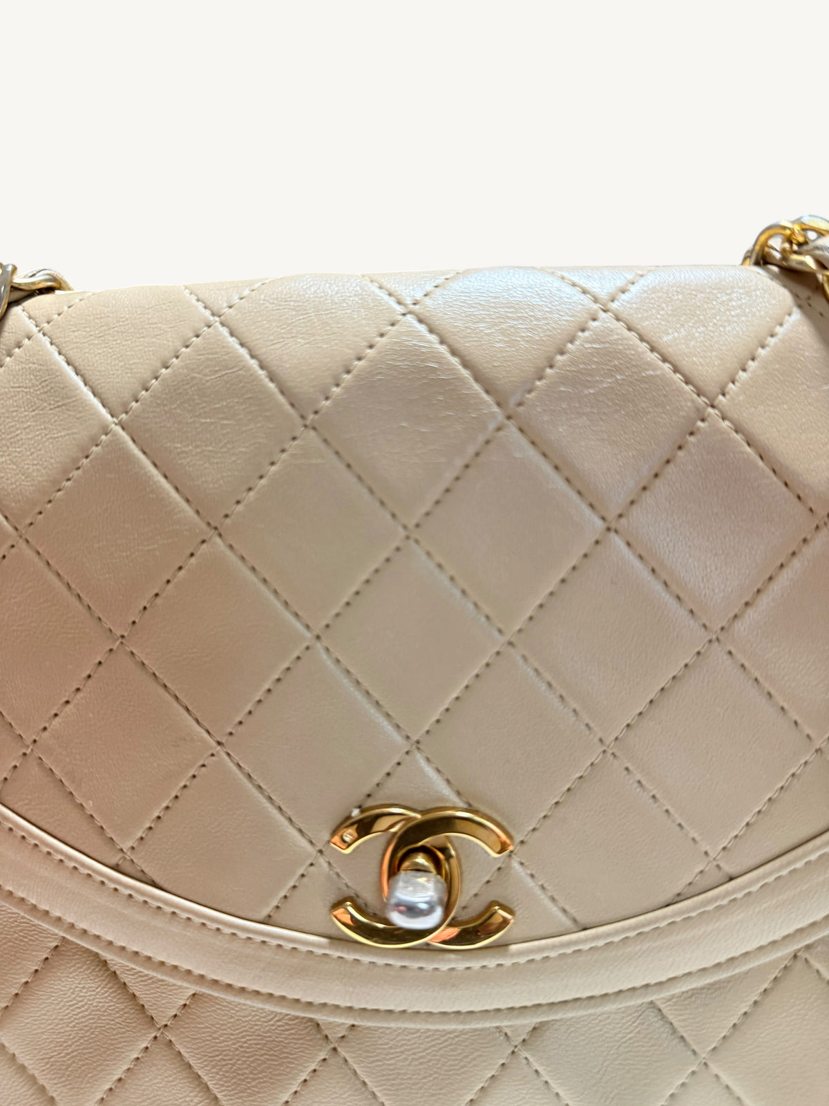 Close-up of a quilted cream-colored Chanel leather handbag with a gold-tone interlocking CC logo clasp on a white background.