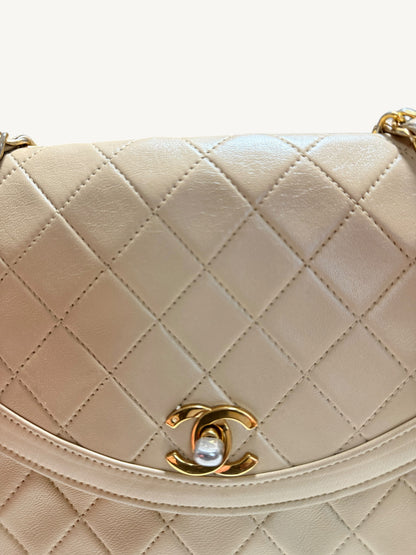 Close-up of a quilted cream-colored Chanel leather handbag with a gold-tone interlocking CC logo clasp on a white background.