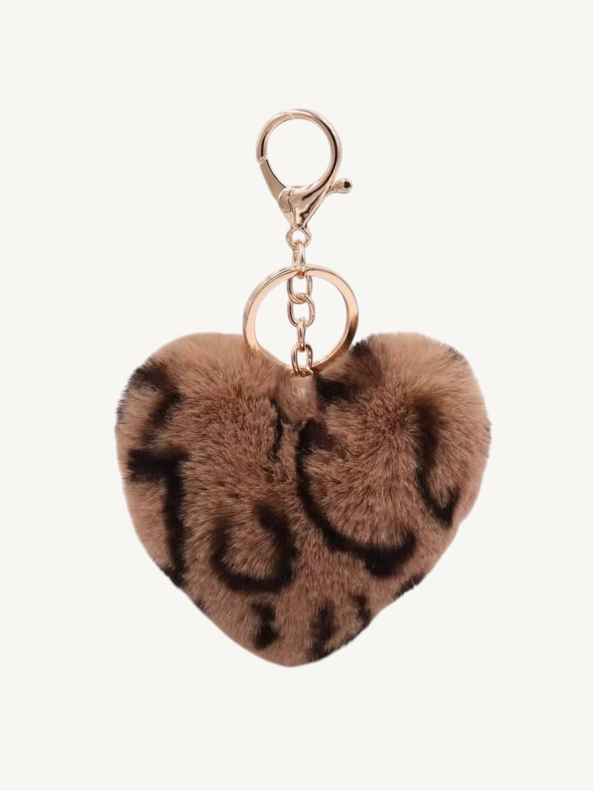 A heart-shaped faux fur keychain in a brown and black leopard print pattern, attached to a rose gold metal clasp and keyring, on a light off-white background.