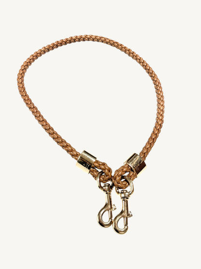 A camel brown Gucci  braided leather dog leash with gold-toned metal hardware, including two snap hooks, shown on a light off-white background.