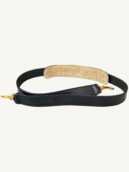 A black leather shoulder strap with a beige suede or shearling-style padded section and gold-tone metal hardware, shown on a plain light background.
