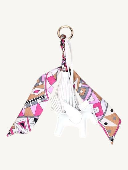 A fashion accessory keychain featuring a white faux leather horse charm, white tassels, and a geometric patterned fabric wing in pink, beige, black, and white, attached to a gold-tone ring.
